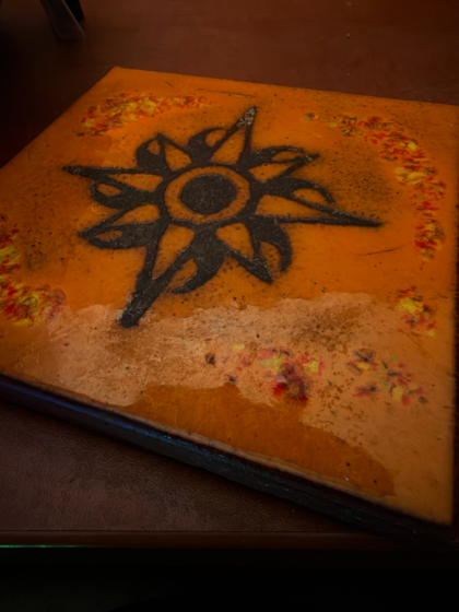 a hand-crafted tile of a sun on a desk acting as a coaster